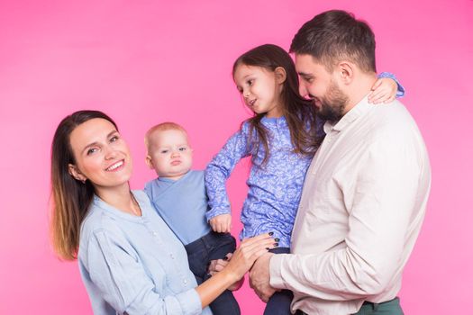 Cute family posing and smiling at camera together on pink background.