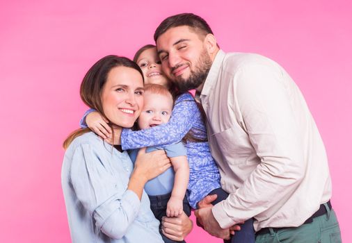 Cute family posing and smiling at camera together on pink background.