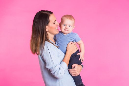 Loving mother playing with her baby boy on pink background.