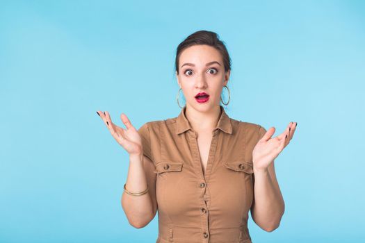 shocked young woman, isolated against blue studio background.