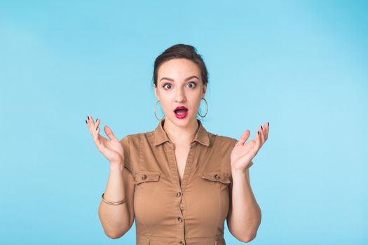 shocked young woman, isolated against blue studio background.