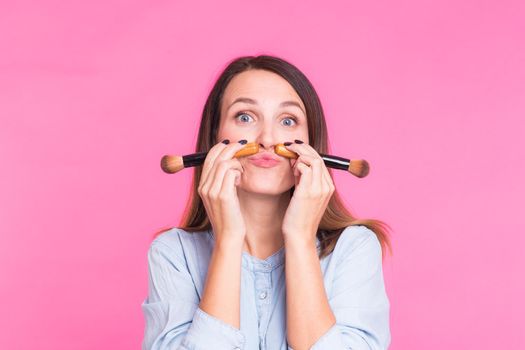 Funny makeup artist with brushes on pink background.