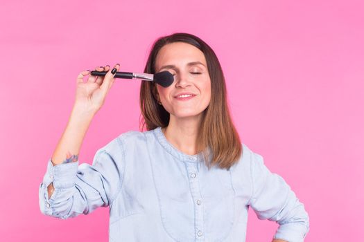 Beautiful young woman applying cosmetic powder on her face with tassel, skin care concept.