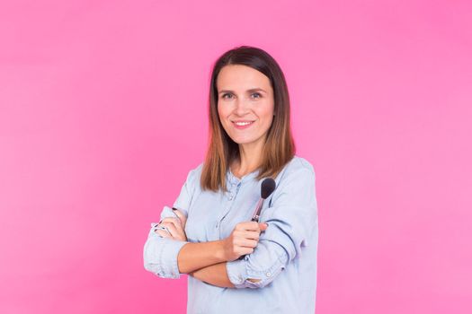 Portrait of makeup artist with brushes in hand on a pink background