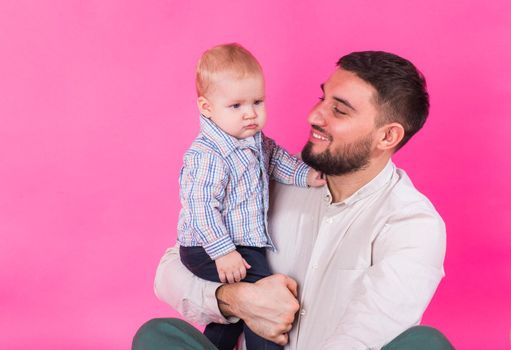 Happy father with his baby son on pink background.