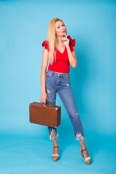 Summer, travel, people and holidays concept - fashionable young blond woman with retro suitcase isolated on blue background.