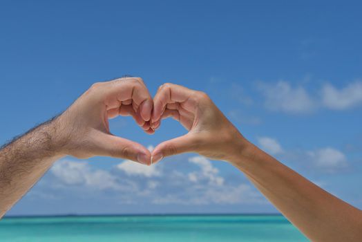 romantic couple make heart shape symbol of love with arms on sunny tropical beach and sea in background