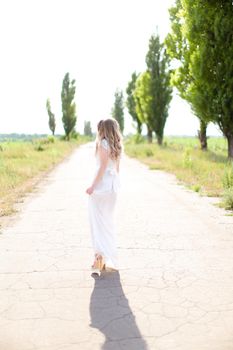 Back view of american bride wearing white dress walking on road. Concept of wedding photo session and fiancee.