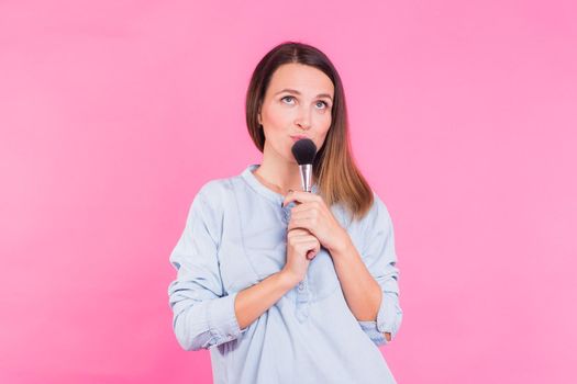 Professional makeup artist with brushes on pink background.