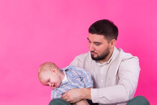 happy father with a baby son isolated on a pink background.