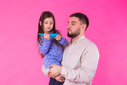 Happy father holding baby daughter in hands over pink background.