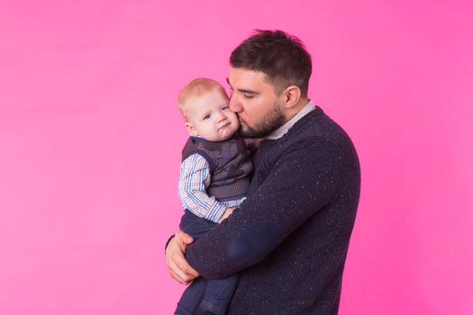 Happy father holding baby son in hands over pink background.