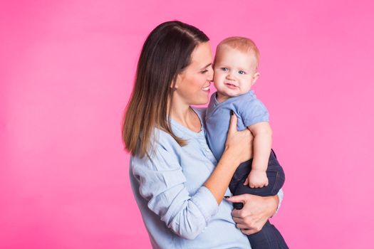 Loving mother playing with her baby boy on pink background.