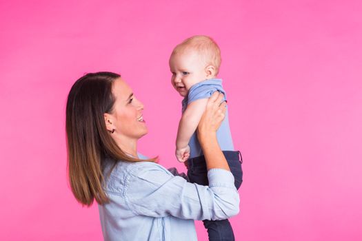 Loving mother playing with her baby boy on pink background.