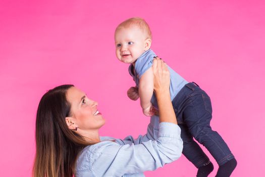 Loving mother playing with her baby boy on pink background.