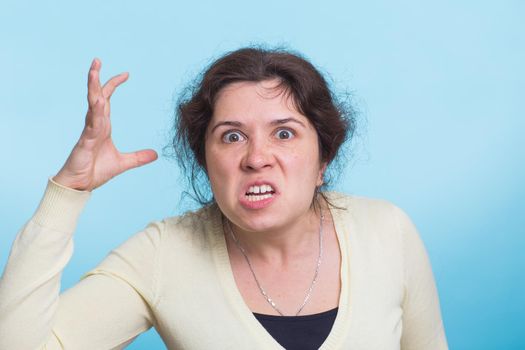 Angry aggressive woman with ferocious expression on blue background.