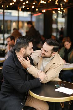 Caucasian european gays sitting at street cafe and hugging. Concept of relationship and same sex couple.