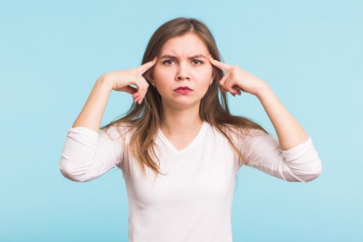 Portrait of beautiful young woman with bare shoulders touching her temples feeling stress, on blue background.