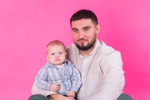 happy father with a baby son isolated on a pink background.