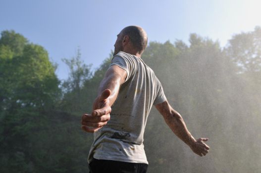 standing man with wide opened arms with waterfalls in background and representing freshness healthy lifestyle and success concept