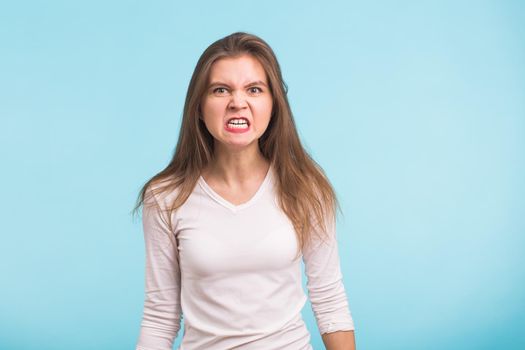 portrait of young angry woman on blue background.