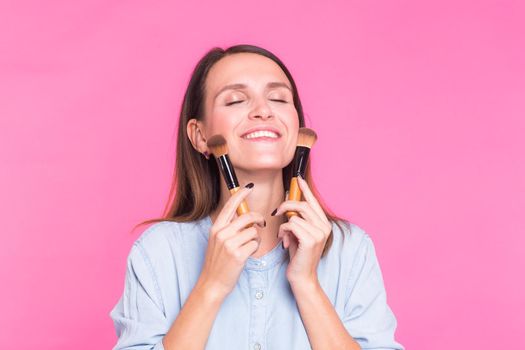 Professional makeup artist with brushes on pink background.