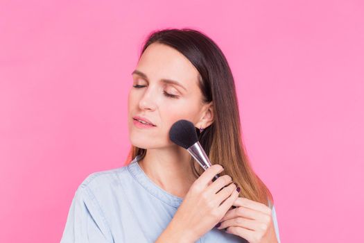 Beautiful young woman applying cosmetic powder on her face with tassel, skin care concept.