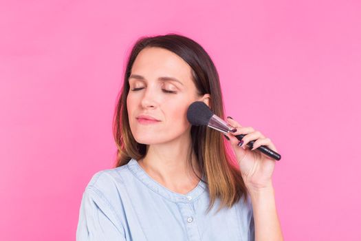 Portrait of makeup artist with brushes in hand on a pink background