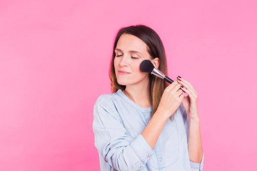 Professional makeup artist with brushes on pink background.