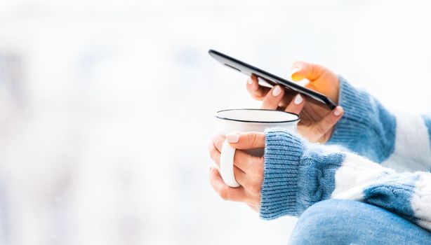 Cup and smartphone in female hands close up