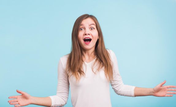 Surprised young woman shouting over blue background. Looking at camera.