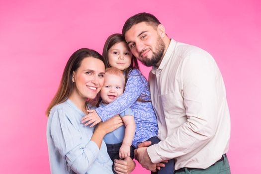 Cute family posing and smiling at camera together on pink background.