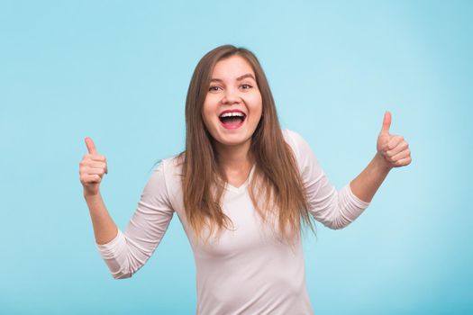 Happy young woman giving thumbs up on blue background.