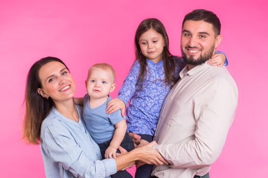 Cute family posing and smiling at camera together on pink background.