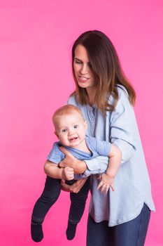 family, motherhood, parenting, people and child care concept - happy mother holds adorable baby over pink background.