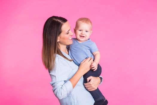 happy young mother with a baby child on pink background.