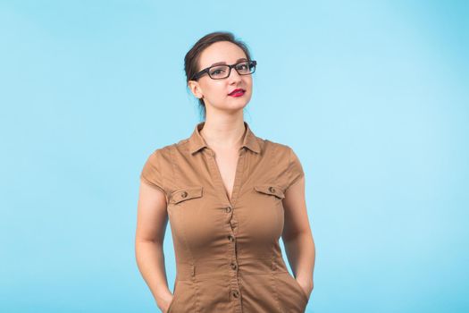 Elegant cheerful brunette in eyeglasses smiling at camera on blue background.