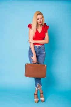 Summer, fashion and holiday concept - Beautiful blonde woman with retro suitcase on blue background.