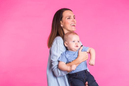 Loving mother playing with her baby boy on pink background.