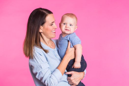 happy young mother with a baby child on pink background.