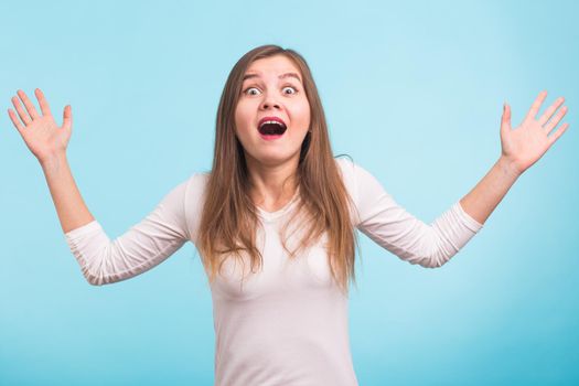 Surprised young woman shouting over blue background. Looking at camera.