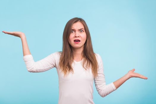 Portrait of a young woman shrugging shoulders over blue background.