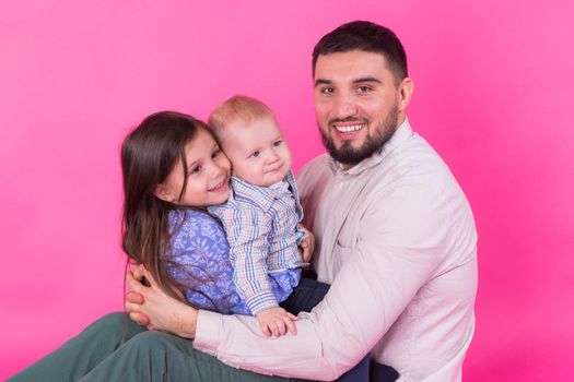 handsome father carrying his little daughter and baby son on pink background.