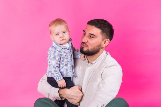 Happy portrait of the father and son on pink background. In studio.