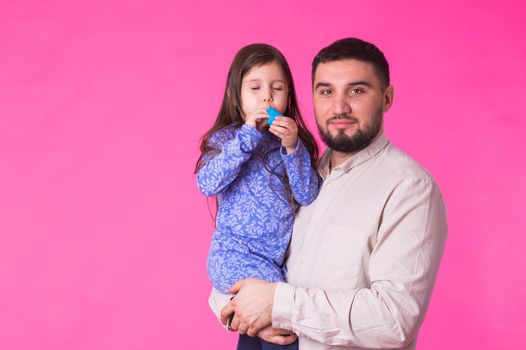 Happy father holding baby daughter in hands over pink background.
