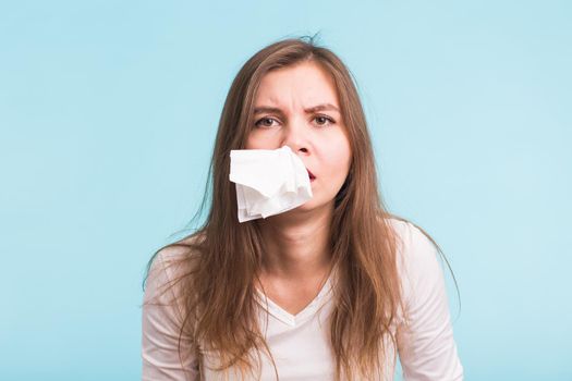 Young woman has a runny nose on blue background.