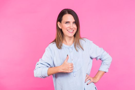 Portrait of a beautiful woman with long brown hair wearing blue cotton blouse, standing waist up smiling on a pink background.