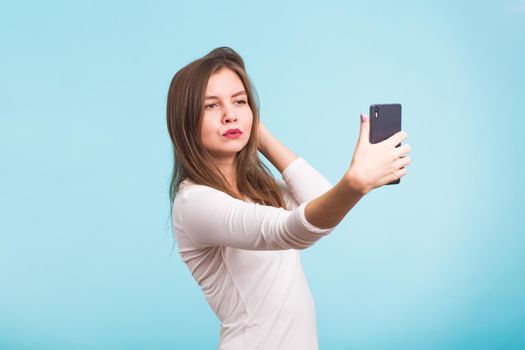 Joyful young women making selfie by her smart phone on blue background.