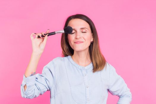 Professional makeup artist with brushes on pink background.