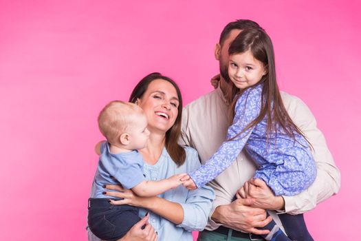 Cute family posing and smiling at camera together on pink background.